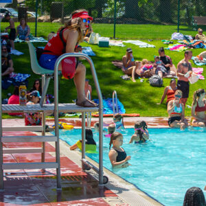 Woman lifeguard in high chair overlooking pool users