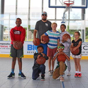 Youth recreation leader and group of children with basketballs on court