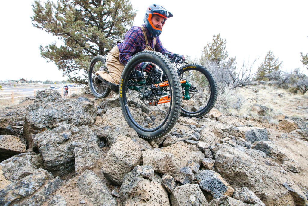 a cyclist on an adaptive bike crosses a lava rock pile obstacle on the skills course