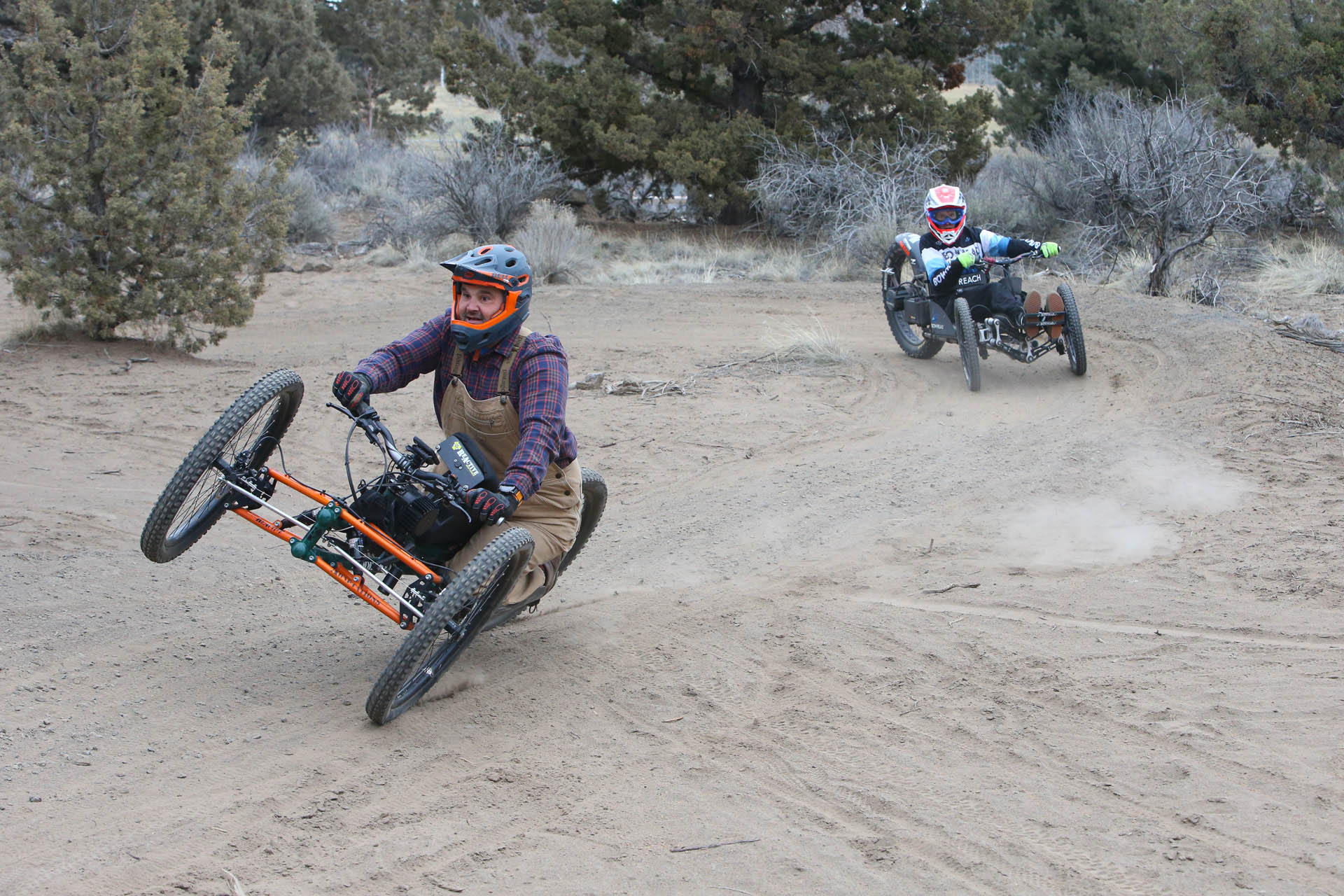 two cyclists on adaptive bikes ride through corners on the natural surface skills course