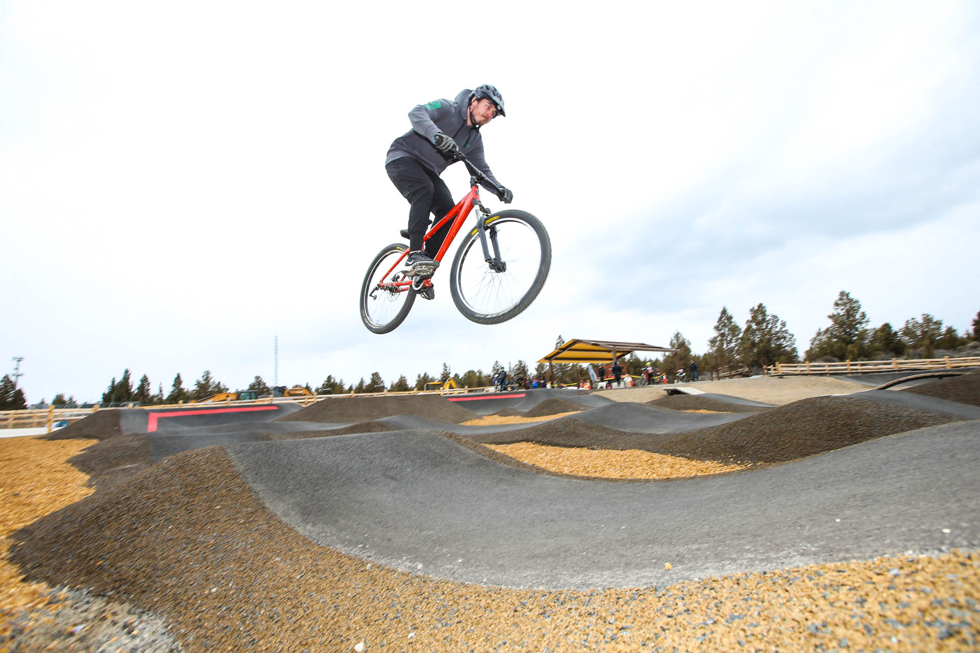 an adult on a bike launches into the air above the pump track