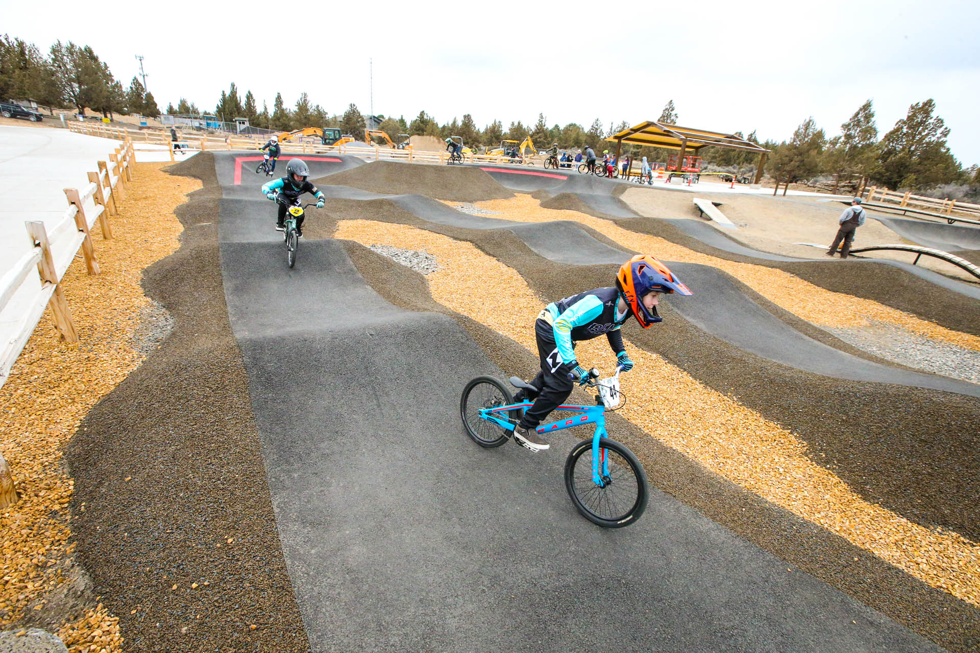 wide image of pump track with several bike riders throughout the course