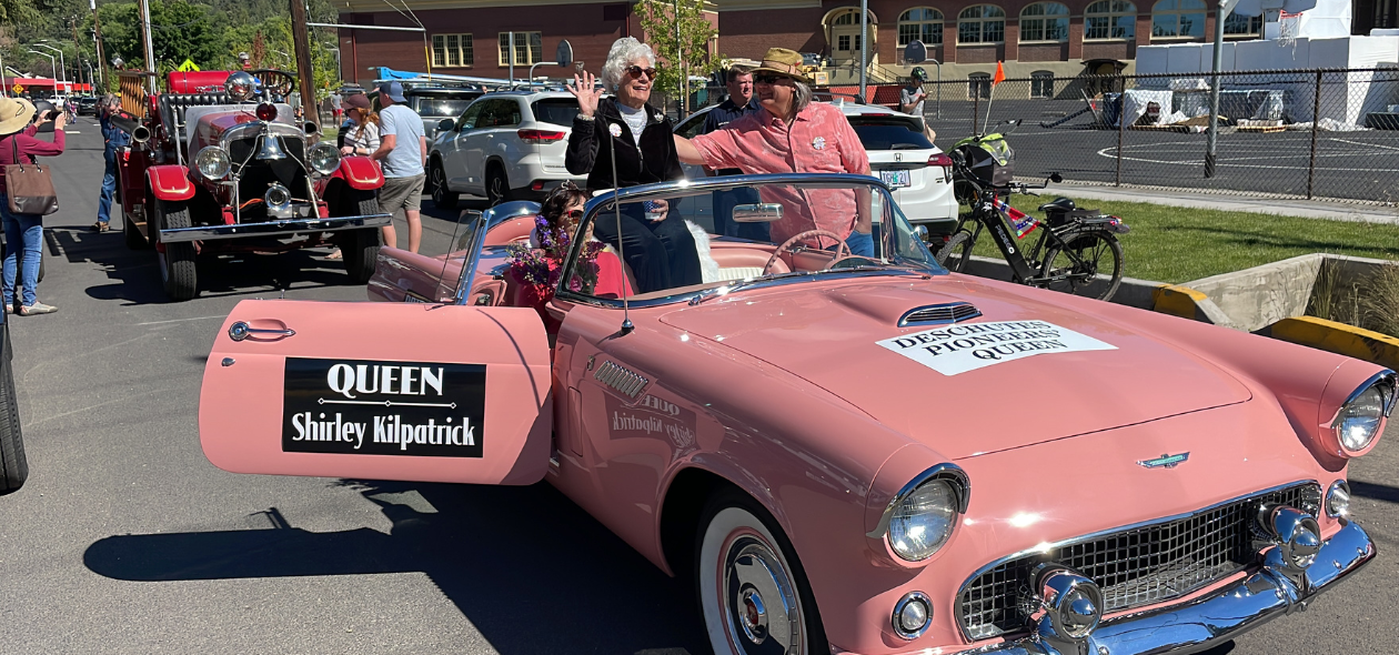 parade Queen rides through the parade route in a pink car. Old-fashion fire engine in background