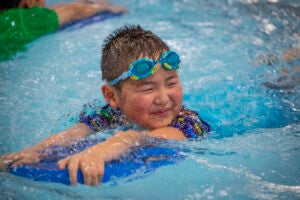 A young child smiles while using a floatation device during swim lessons.