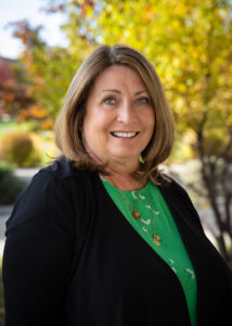 Photograph of Deb Schoen looking directly forward with trees in the background.