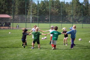 Group of children hold hands in a circle as they play togethr during BPRD sports camp at Skyline.