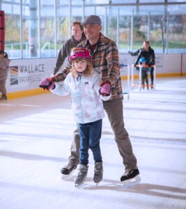 adult and child hold hands and skate together on the ice rink