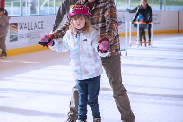 adult and child hold hands and skate together on the ice rink