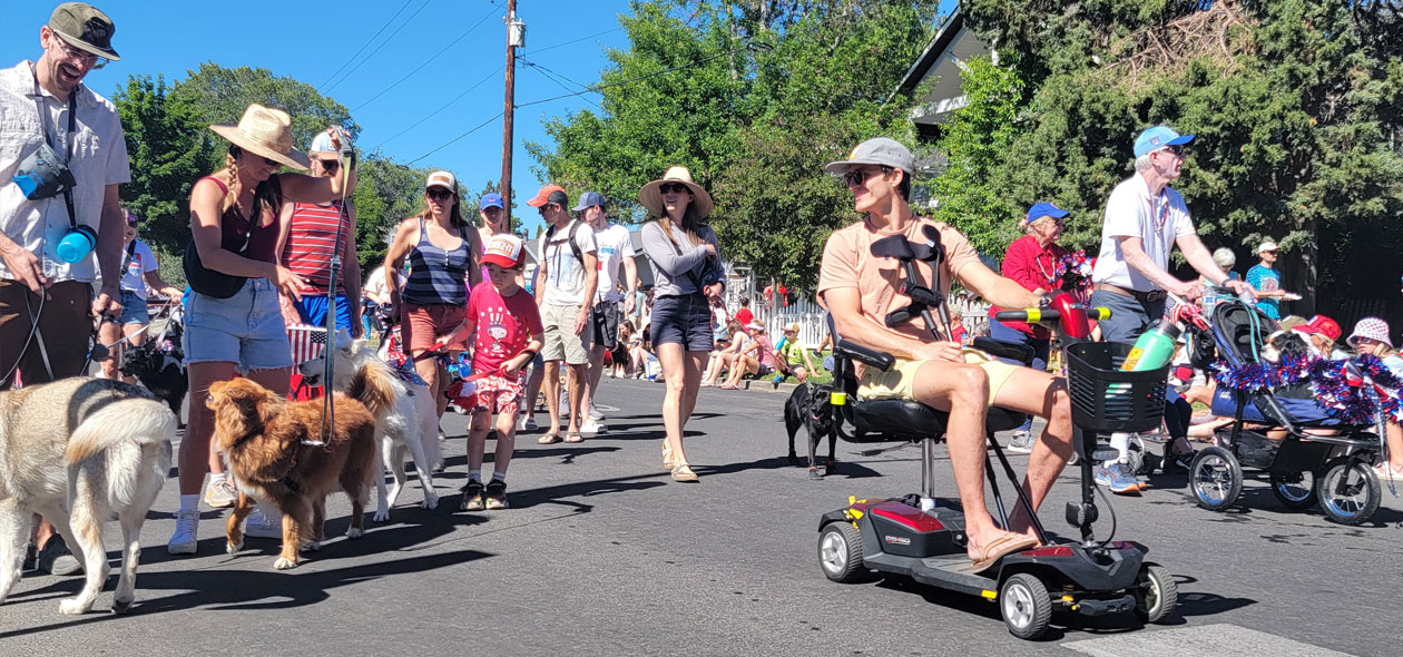 a man on a mobility device leads a group and their pets on the parade route