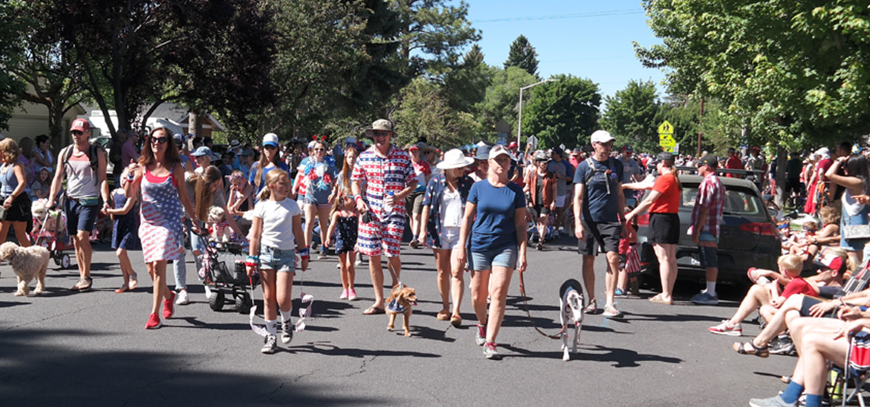stars and stripped decorated participants walk in the parade with their dogs on leashes.