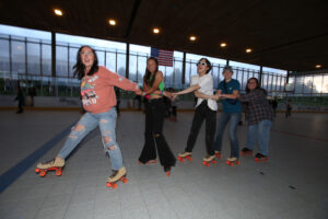 Group of five friends holding on to eachother playfully as they cruise through a roller dance party at the Pavilion.