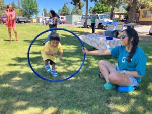 Young boy happily stepping through an upright hoola hoop while other children play nearby