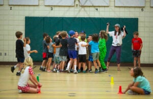 Staff cheers on a group of children embracing and cheering together in a gym at a day camp