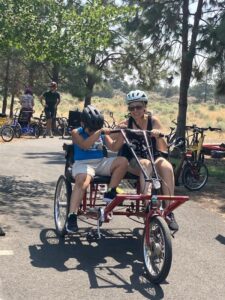 Adaptive cycling with a young user and adult woman helping on a two person bike