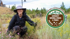 A volunteer smiles at the camera while pulling weeds.