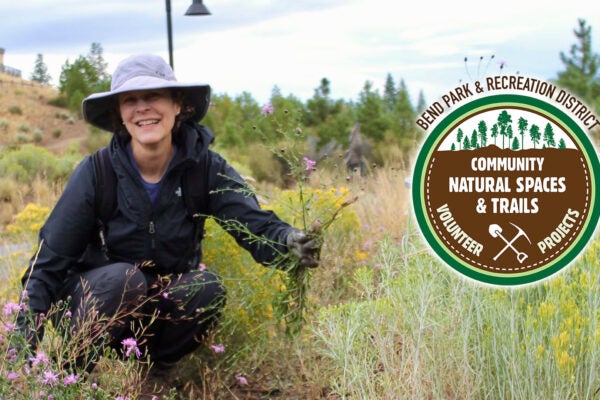 A volunteer smiles at the camera while pulling weeds.