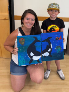A mother and her son psoe with the paintings they made together in a With A Child art class.