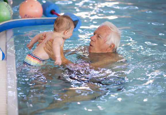 Older adult plays with a young child in the pool at Juniper.