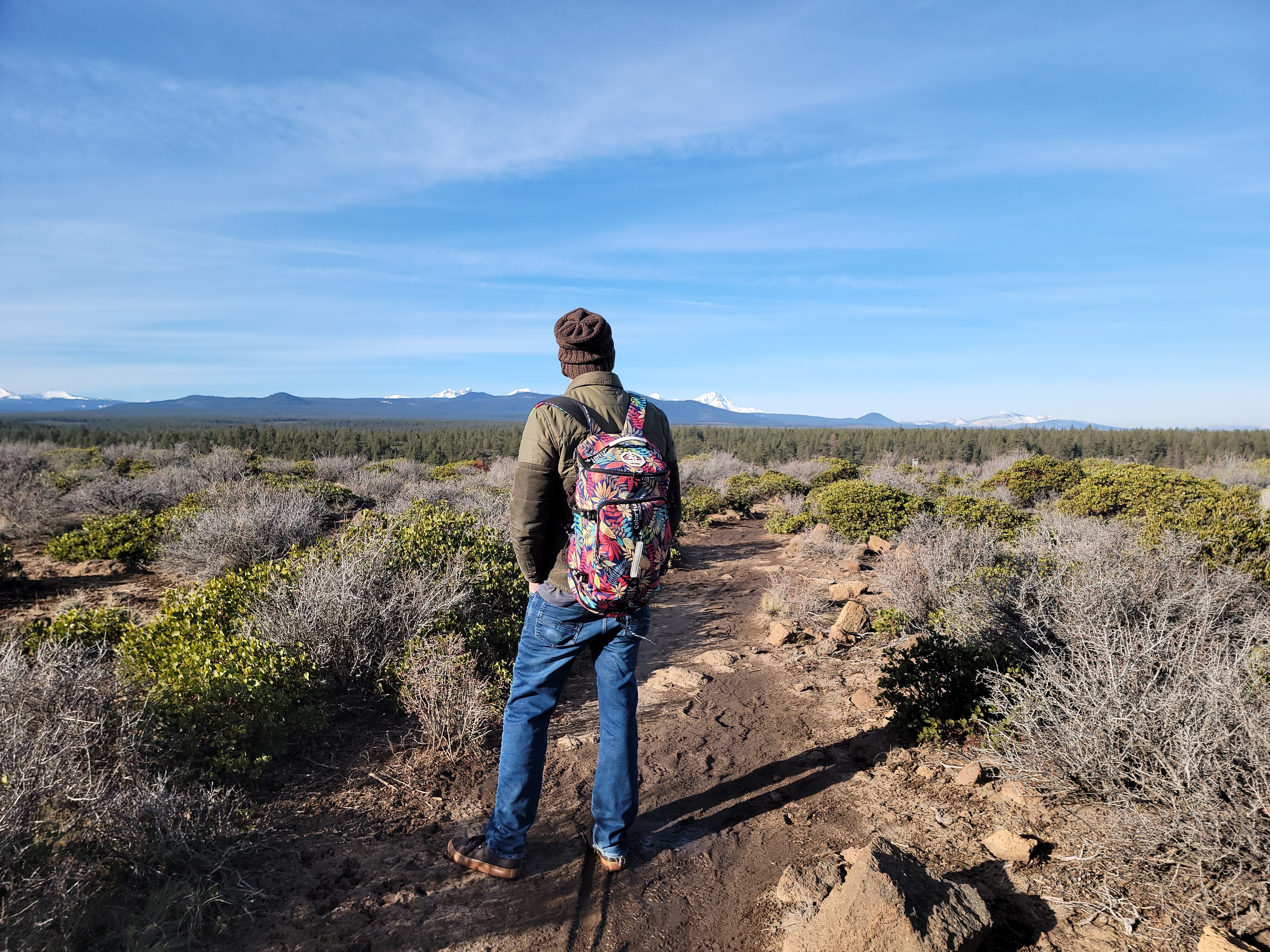 hiker on trail looking across open space toward Cascade mountains