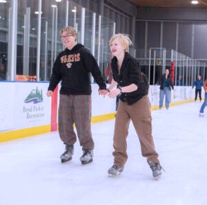 two adult ice skaters hold hands and smile while skating on the ice