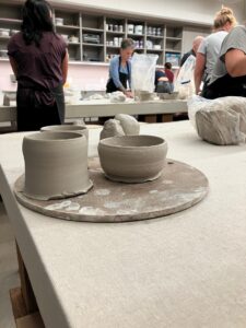four clay pot projects in the foreground of a clay class with people in the background